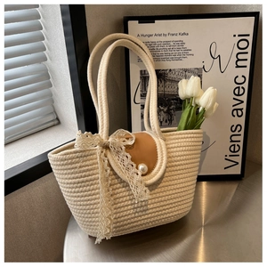 Detailed shot of beige woven tote bag with PU leather patch, pearl, and large lace bow