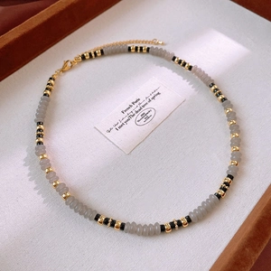 Detail of beaded necklace with grey and black stones and gold spacer beads on cloth