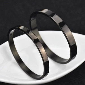 Pair of minimalist polished black titanium steel bracelets on a white ceramic tray