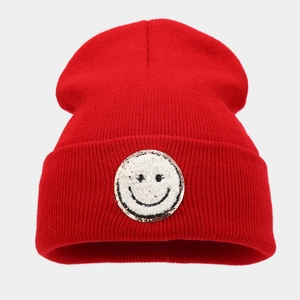 Dettaglio di un berretto in maglia rossa con toppa smiley e bordo dorato scintillante