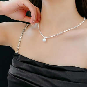 Detail of a silver irregular bead necklace with a white pearl pendant on a model