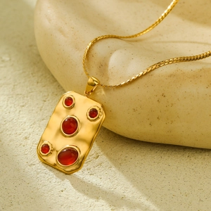 Detail of a gold titanium necklace with five red stones on a rectangular pendant