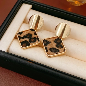 Détail de boucles d'oreilles carrées imprimé léopard avec clous dorés sur boîte à bijoux