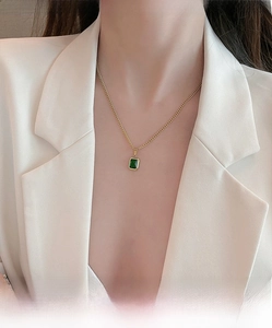 Close-up of gold titanium necklace with emerald pendant worn on business blazer