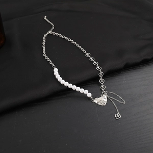 Detail of asymmetric pearl and silver heart chain necklace on black silk and wood