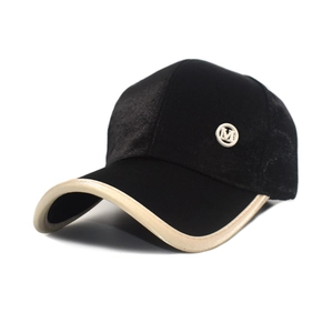 Detailed view of black velvet baseball cap featuring white M logo badge and beige trim