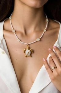 Close-up of golden turtle pendant on pearl necklace with delicate butterfly accents