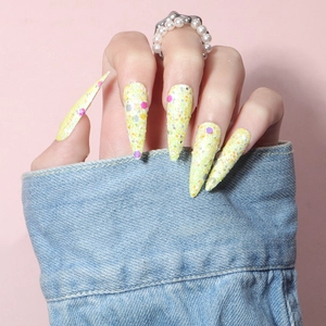 Macro detail of long stiletto press-on nails with yellow glitter and colorful sequins