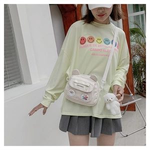 Detail of white canvas crossbody bag with cute bear ears and plush toy pendant