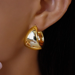Macro view of a model wearing high-polished large golden teardrop earrings in minimalist style