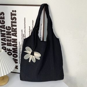 Close-up of black pleated seersucker tote bag with delicate white lace flower charm