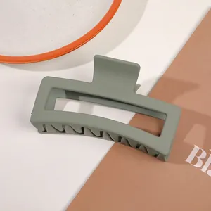 Detail of large sage green matte claw clip with hollow rectangular design on white table
