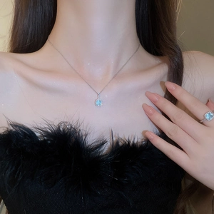 Close-up of a silver necklace featuring a square light blue gemstone pendant on a model