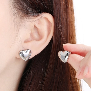Macro shot of polished silver heart stud earrings with smooth metallic finish on model
