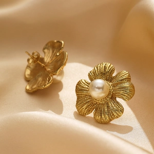 Detailed view of brushed gold flower stud earring with a white pearl on silk fabric