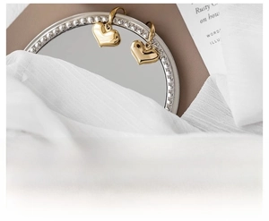 Close-up of golden 316L stainless steel heart earrings hanging on a vintage mirror