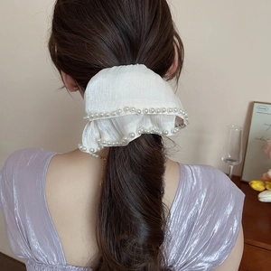 Detail of a large white silk hair bow with pearl edges worn by a model in a cozy room