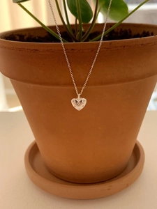 Detail of silver heart necklace with star engravings on a terracotta pot background