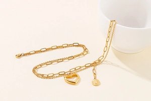 Close-up of golden double-layer chain necklace with heart pendant and coin on ceramic cup