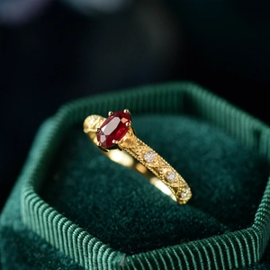 Macro shot of an oval red gemstone gold ring with side engraving in a green velvet box