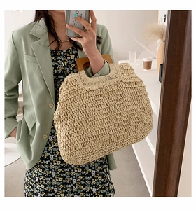 Detail of a large straw tote bag featuring woven texture and round wooden handles