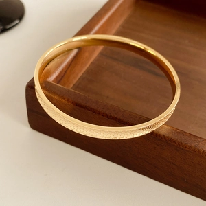 Detail of gold circular bracelet featuring intricate honeycomb textured surface on wooden tray