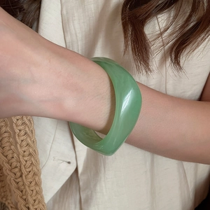Detail of a thick green resin bangle with translucent jade-like finish on female wrist