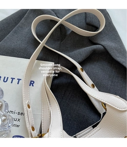 Detail of white lychee grain leather bucket bag with gold rivets and smooth strap