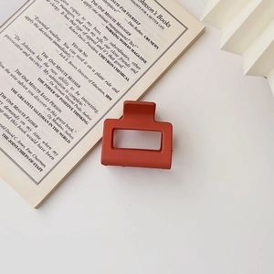 Detail of a minimalist square matte red-brown hair claw clip on an open book background