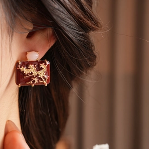 Close-up of vintage enamel earring with red base, golden branch and pink bead detail