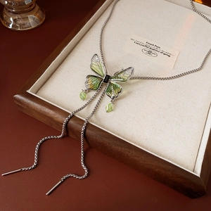 Detail of a green enamel butterfly bolo necklace with rhinestones on a wooden tray