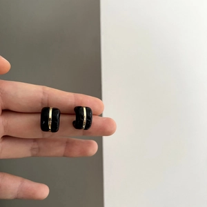 Detail of minimalist C-shaped earring in black enamel with a thin gold metallic stripe