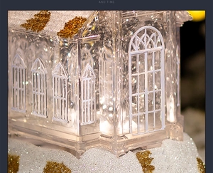 Close-up of a lit crystal church music box with golden glitter snow and warm LED glow