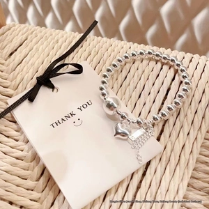 Polished silver beaded bracelet with heart pendant on woven background detail