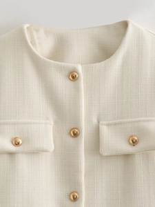 Detailed view of cream tweed jacket featuring textured fabric and gold dome buttons