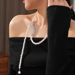 Detail of a pearl necklace featuring a large zircon-studded silver feather pendant and drop pearl