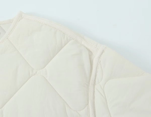Detail of round neckline and diamond quilted pattern on off-white padded jacket