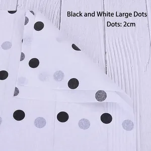 Close-up of 2cm black polka dot floral wrapping paper on a white textured wood background