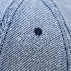 Gros plan détaillé des œillets de ventilation brodés sur la casquette en denim lavé
