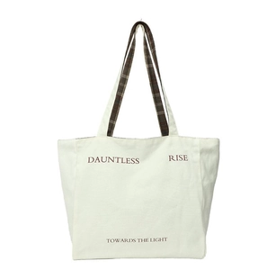 Close-up of cream canvas tote bag featuring Dauntless print and plaid shoulder straps