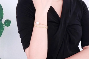 Detail of a golden double-layer bracelet with a white pearl and a clover charm on wrist