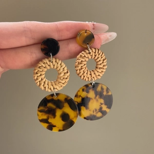 Detail shot of boho earrings featuring amber resin studs and woven rattan circular pendants
