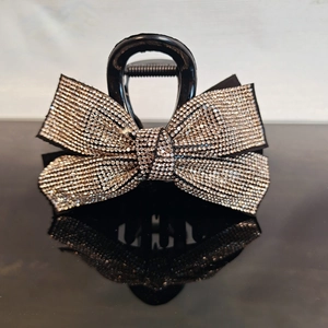 Macro shot of a black bow hair claw clip with sparkling rhinestones on a glossy surface