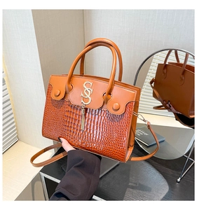 Detail of brown leather handbag with crocodile pattern texture and gold tassel charm