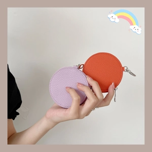 Hand holding round purple and orange leather coin purses with silver metal clips