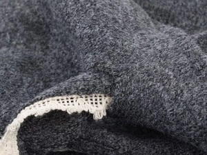 Detail of dark grey knit fabric with white lace trim and bow accent on the cardigan