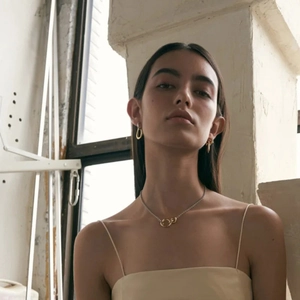 Detail shot of a model wearing two-tone interlocking rings necklace and gold oval earrings