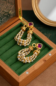 Detailed shot of vintage gold woven earrings with purple gems and white pearls on velvet