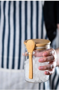 Close-up of glass storage jar with wooden lid and spoon holding white sugar cubes