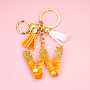 Detail of a letter W resin keychain with orange corn kernels, gold foil, and dual tassels